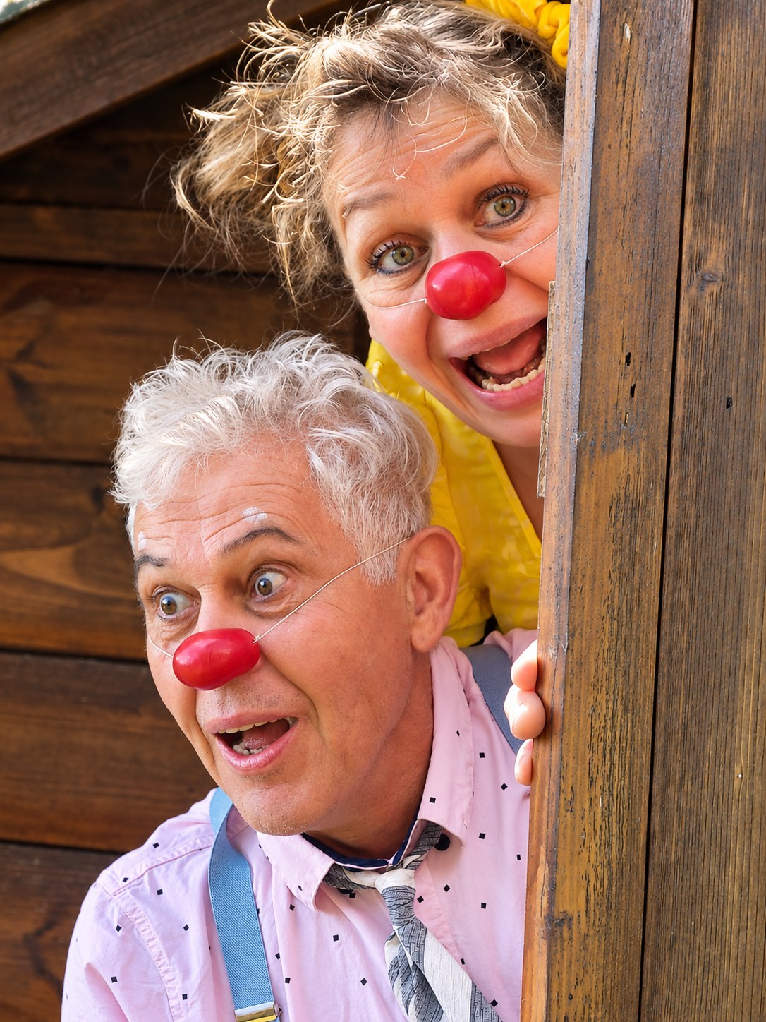 Das Clownduo schaut mit großen Augen um einen hölzernen Türrahmen.
